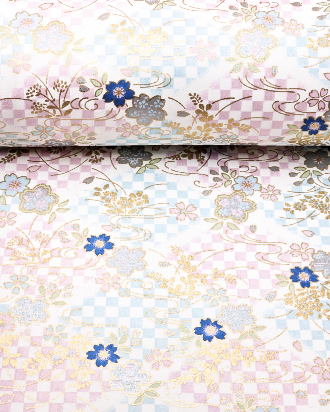 Japanese chiyogami paper featuring blue, pink, and metallic silver cherry blossoms on a blue and purple ichimatsu (checkered) background with metallic gold details, shown rolled to highlight the design.