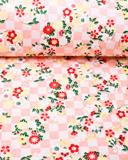 Japanese chiyogami paper featuring yellow, red, and white flowers with green leaves on a light orange ichimatsu (checkered) background with metallic gold accents.