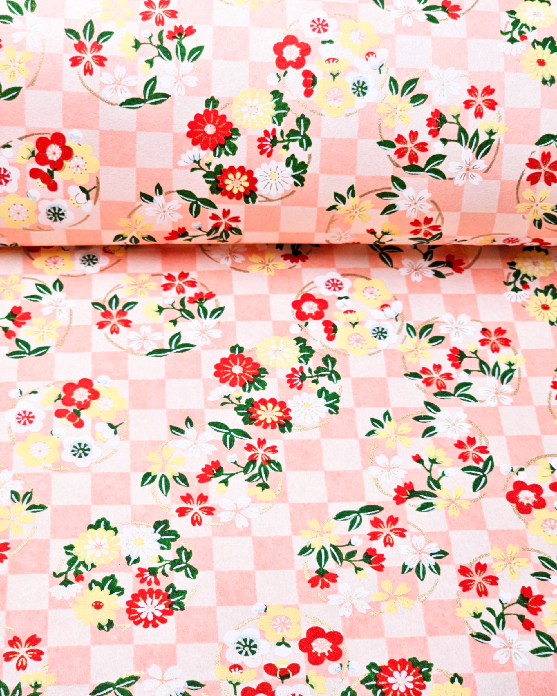Japanese chiyogami paper featuring yellow, red, and white flowers with green leaves on a light orange ichimatsu (checkered) background with metallic gold accents.