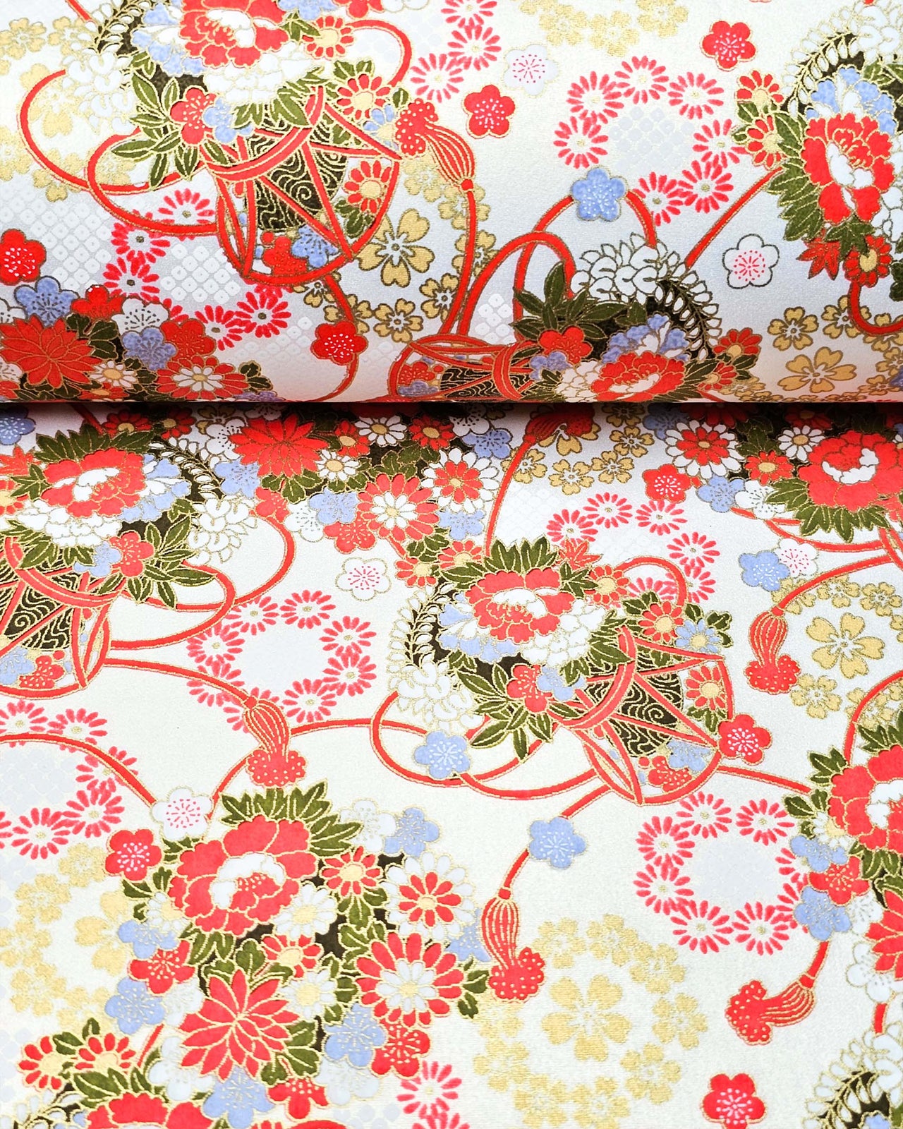 Japanese chiyogami paper featuring assorted red, light blue, and white flowers with green leaves inside red drums on a pearlescent white background with metallic gold accents. 