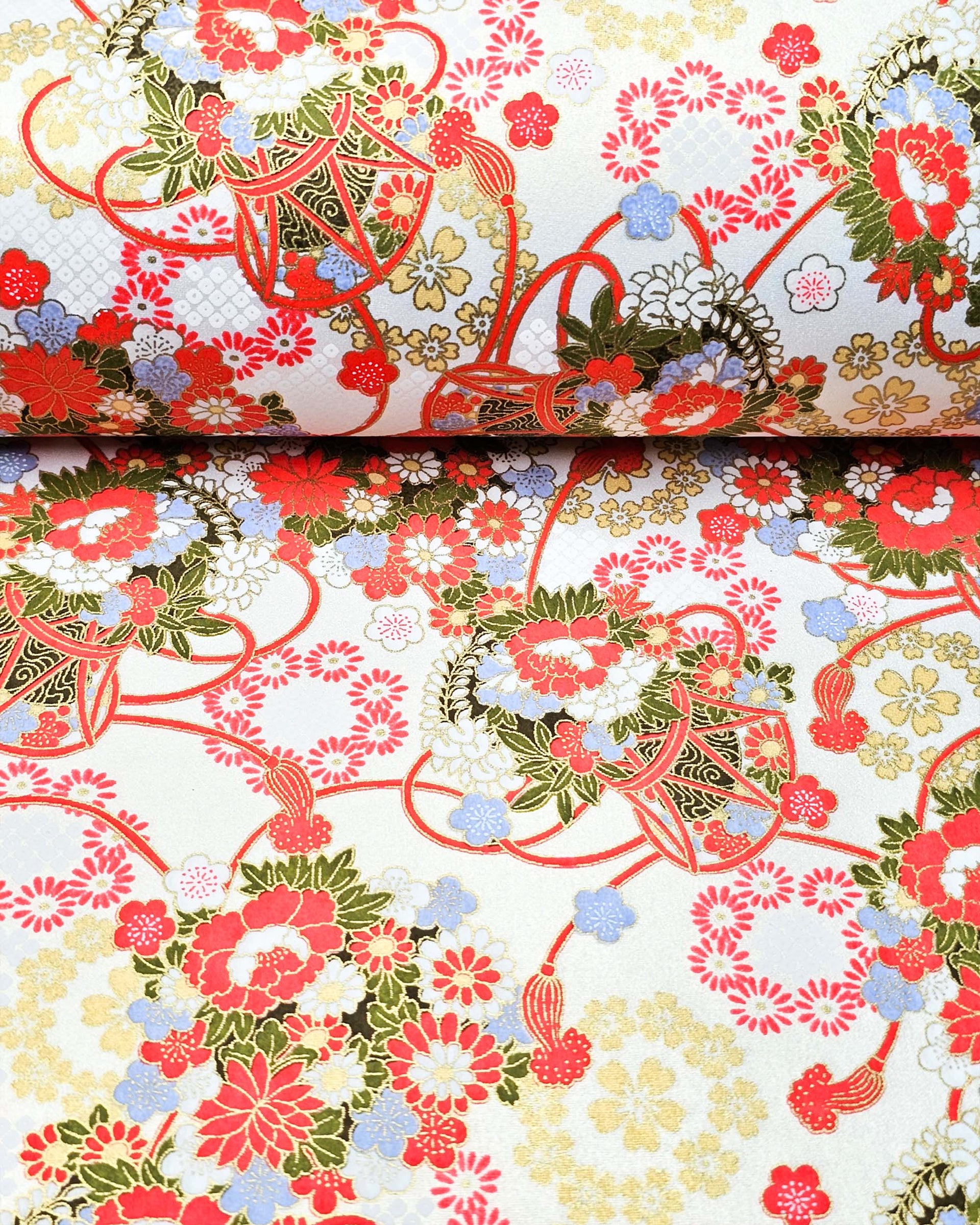 Japanese chiyogami paper featuring assorted red, light blue, and white flowers with green leaves inside red drums on a pearlescent white background with metallic gold accents. 