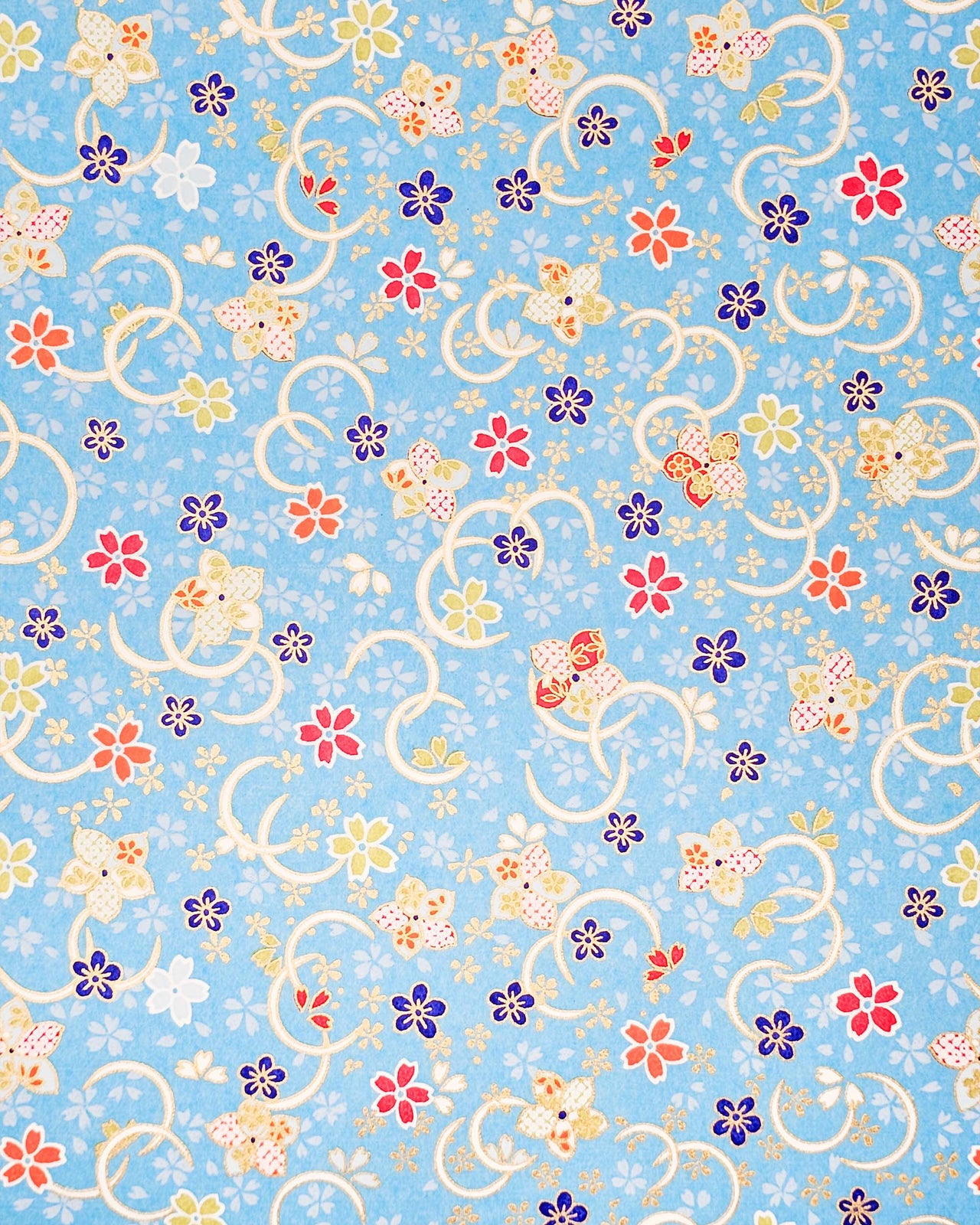Japanese chiyogami paper featuring red, blue, green, and white plum and cherry blossoms on a sky blue background with metallic gold accents.