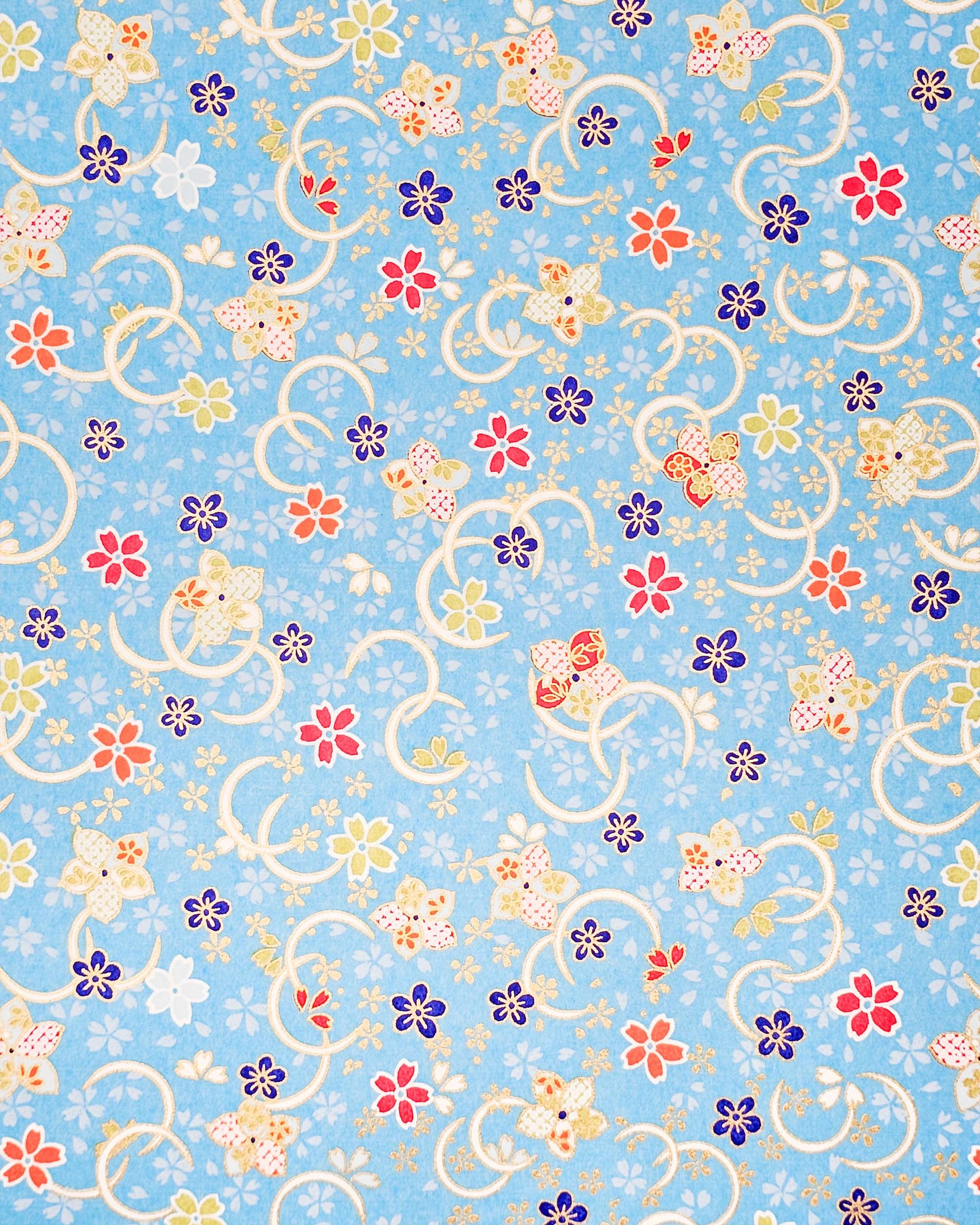 Japanese chiyogami paper featuring red, blue, green, and white plum and cherry blossoms on a sky blue background with metallic gold accents.