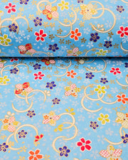 Japanese chiyogami paper featuring red, blue, green, and white plum and cherry blossoms on a sky blue background with metallic gold accents.