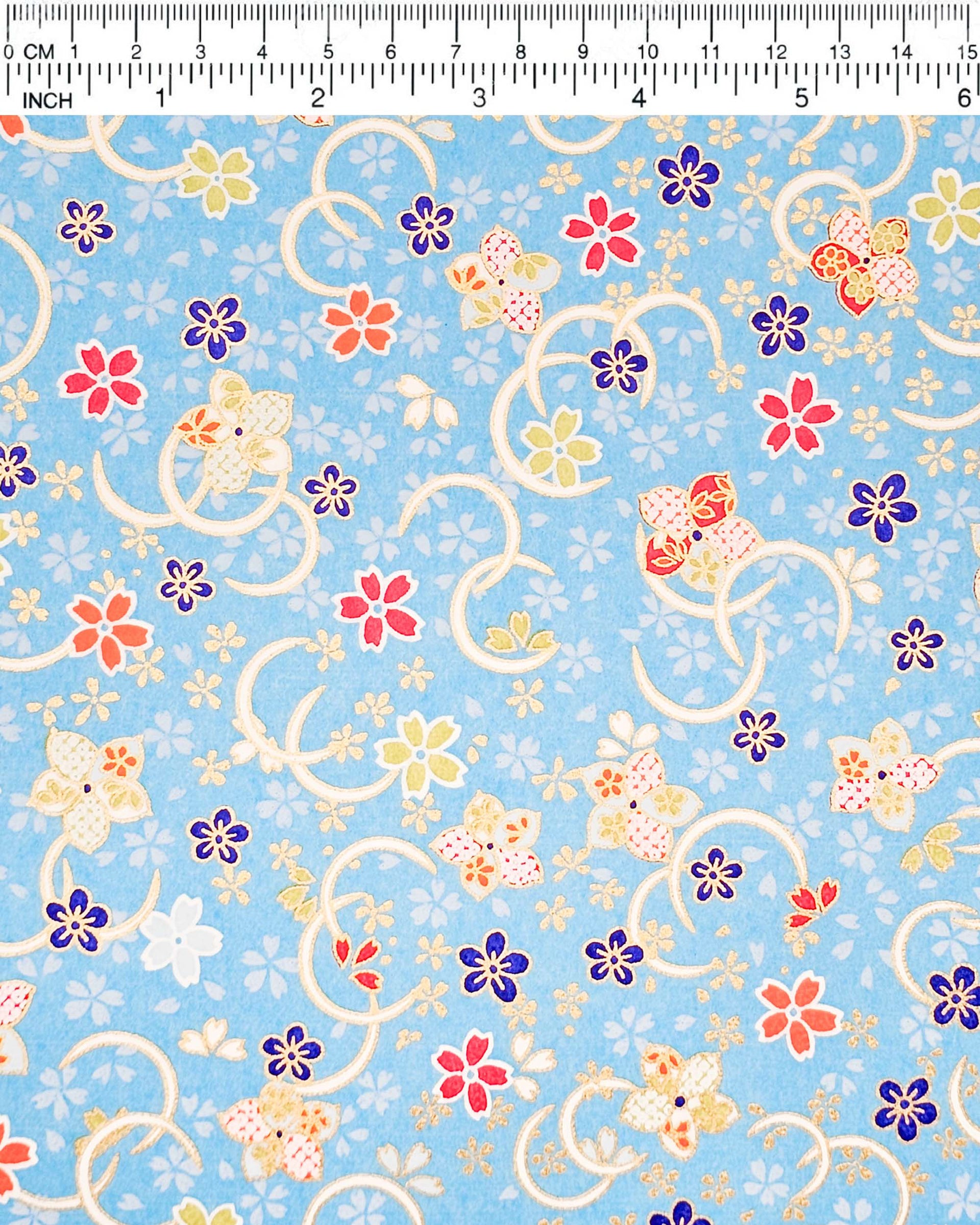 Japanese chiyogami paper featuring red, blue, green, and white plum and cherry blossoms on a sky blue background with metallic gold accents.