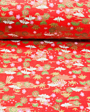 Japanese chiyogami paper featuring small white folded origami cranes with green pine and pink plum blossoms on a red background with metallic gold accents.
