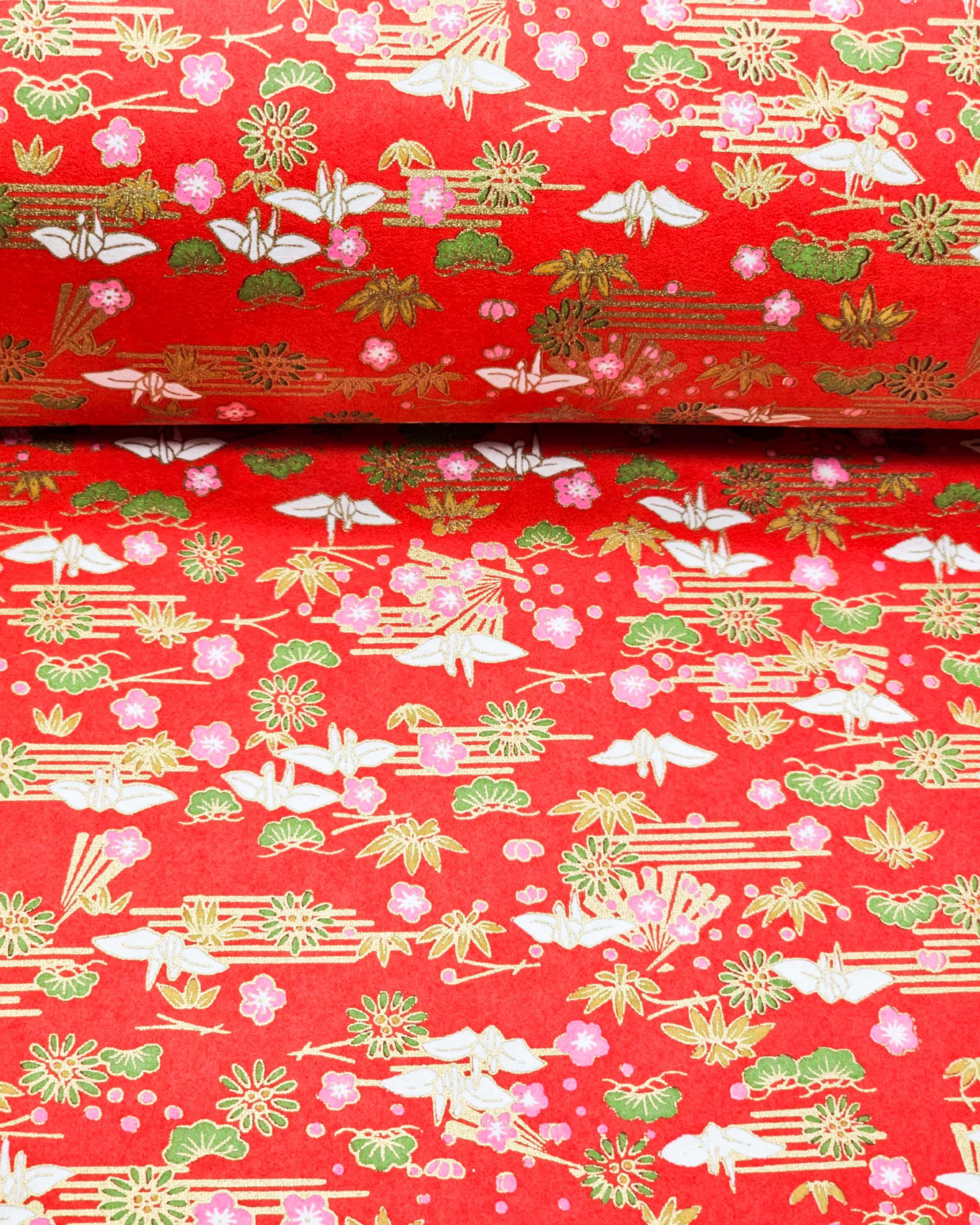Japanese chiyogami paper featuring small white folded origami cranes with green pine and pink plum blossoms on a red background with metallic gold accents.
