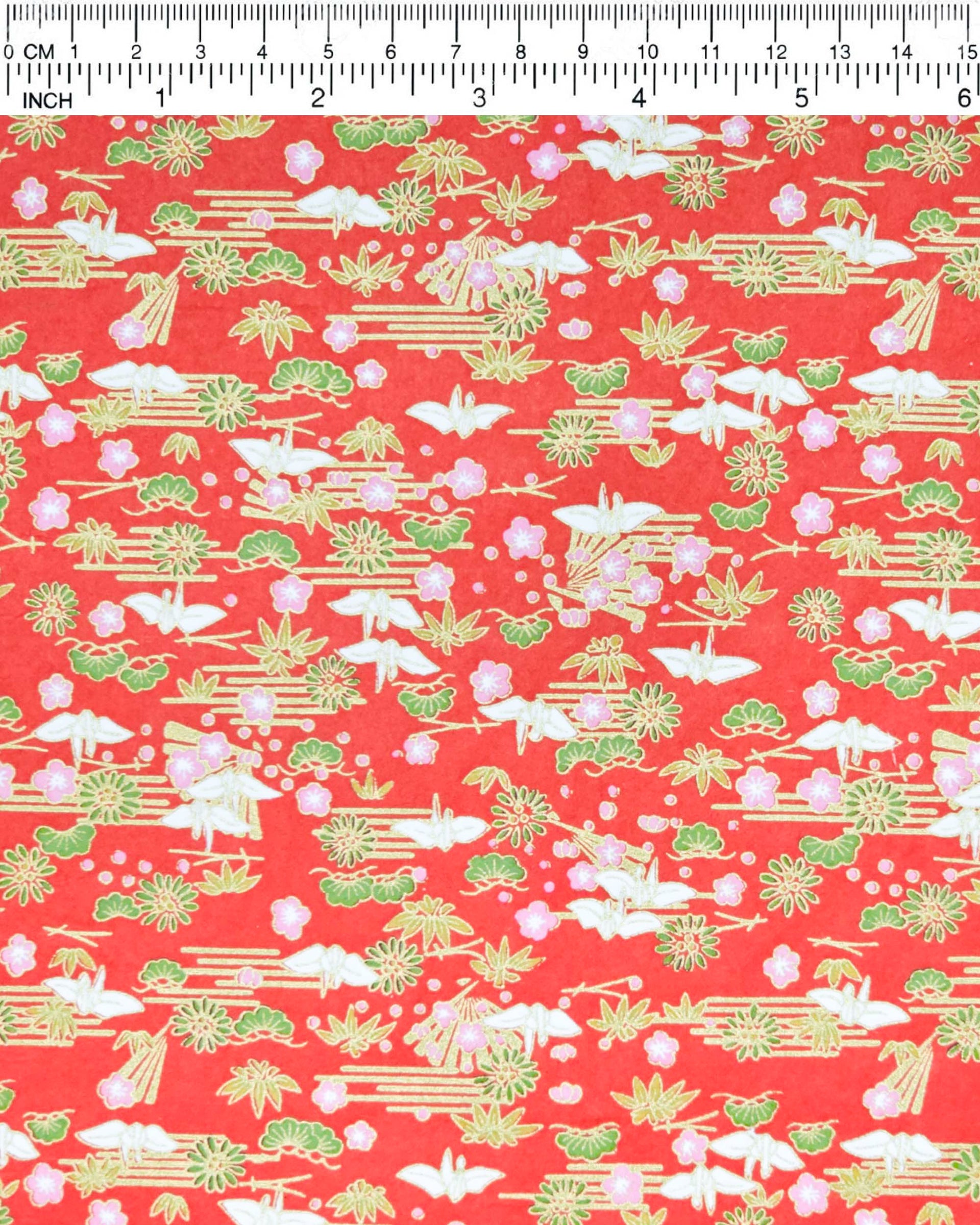 Japanese chiyogami paper featuring small white folded origami cranes with green pine and pink plum blossoms on a red background with metallic gold accents.