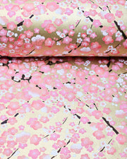 Japanese chiyogami paper featuring pink and white plum blossom trees with dark brown branches on a metallic gold background, shown rolled to highlight the design.