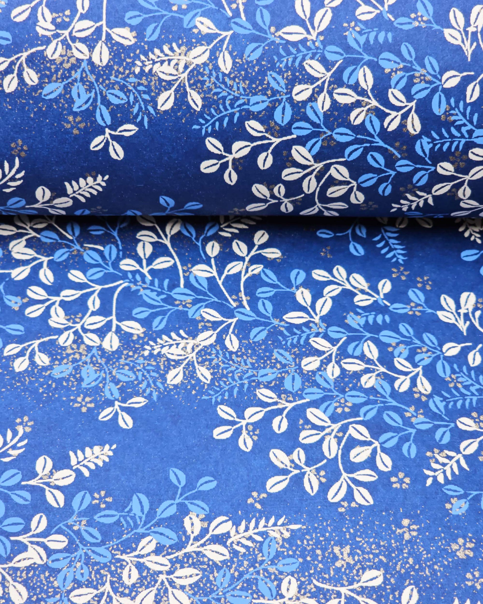 Japanese chiyogami paper featuring blue and white hagi (bush clover) on a blue background with metallic gold details, shown rolled to highlight the design.