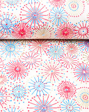 Japanese chiyogami paper featuring colorful red, blue, pink, and white exploding fireworks on a white background with metallic gold details, shown rolled to highlight the design.