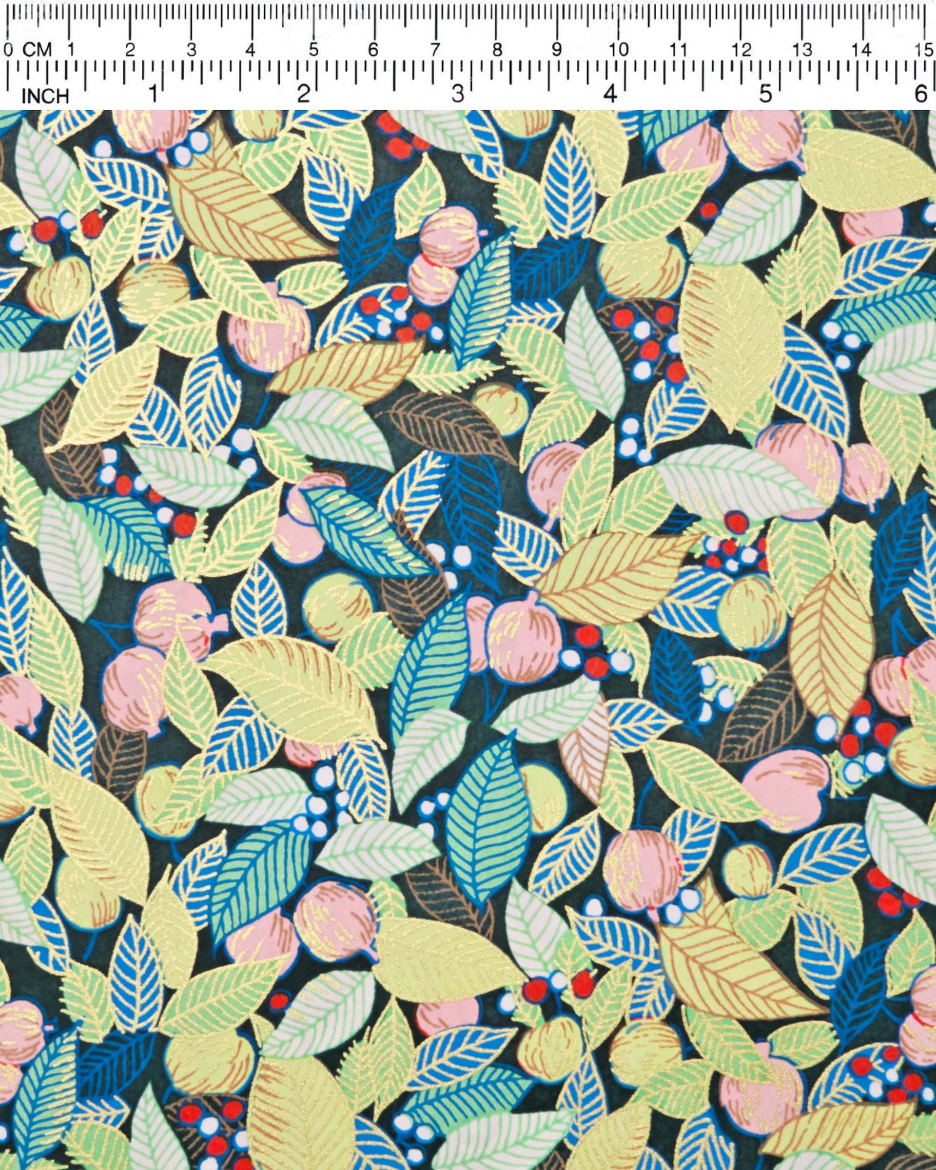 Japanese chiyogami paper featuring green, blue, and yellow leaves with pink persimmon fruits on a dark green background with metallic gold details, shown rolled to highlight the design.