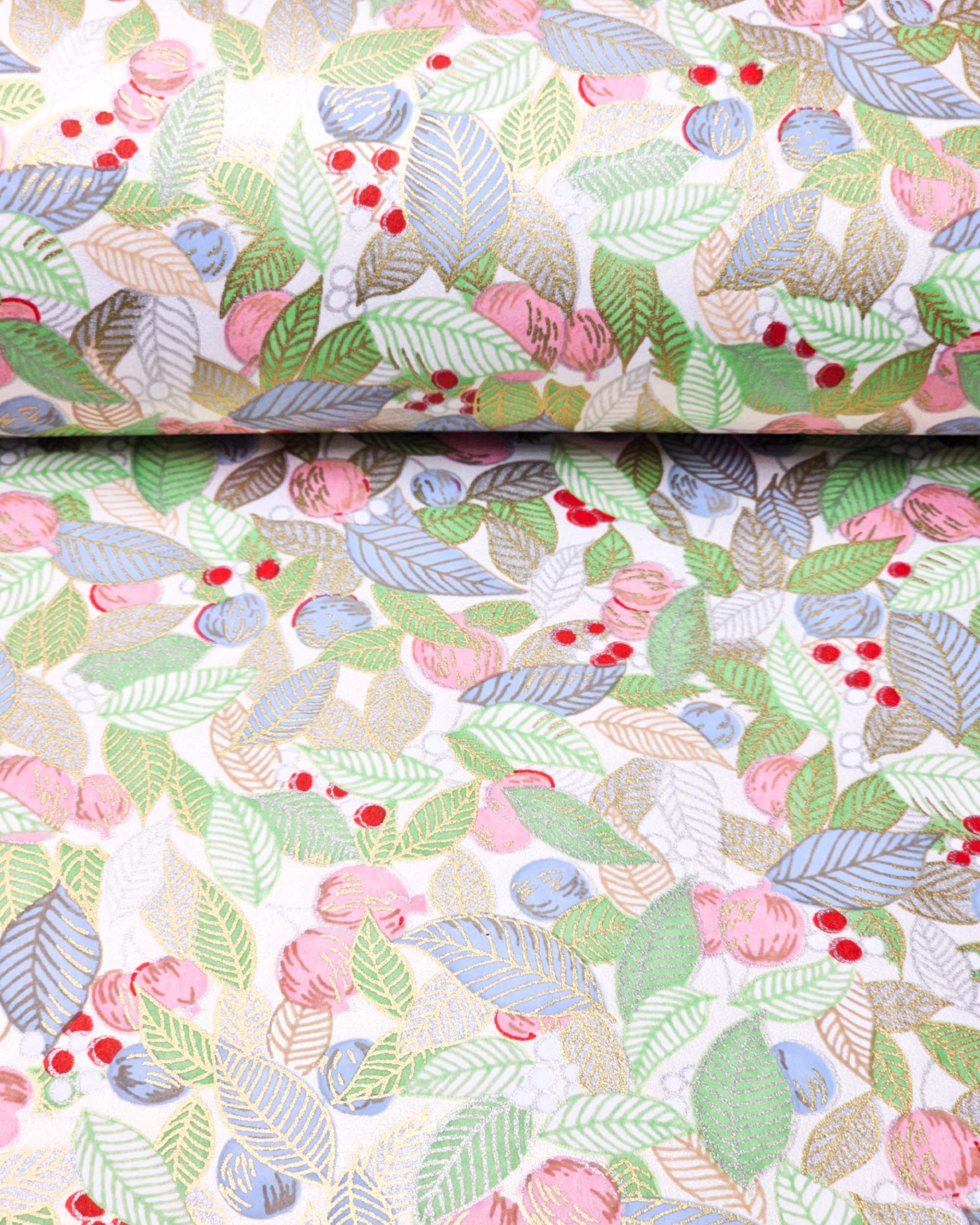 Japanese chiyogami paper featuring green, blue, and silver leaves with pink persimmon fruits on a white background with metallic gold details, shown rolled to highlight the design.