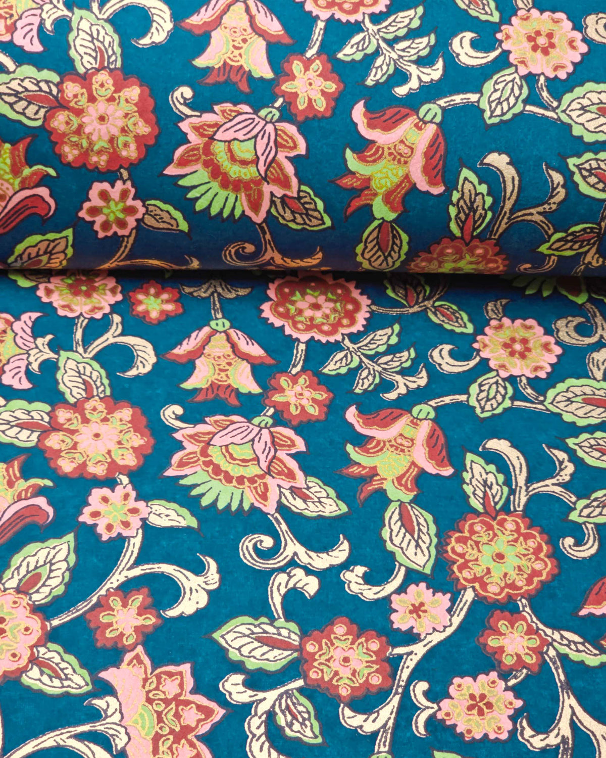 Japanese chiyogami paper featuring red, pink, and green sarasa flowers on a dark blue background with metallic gold details, shown rolled to highlight the design.
