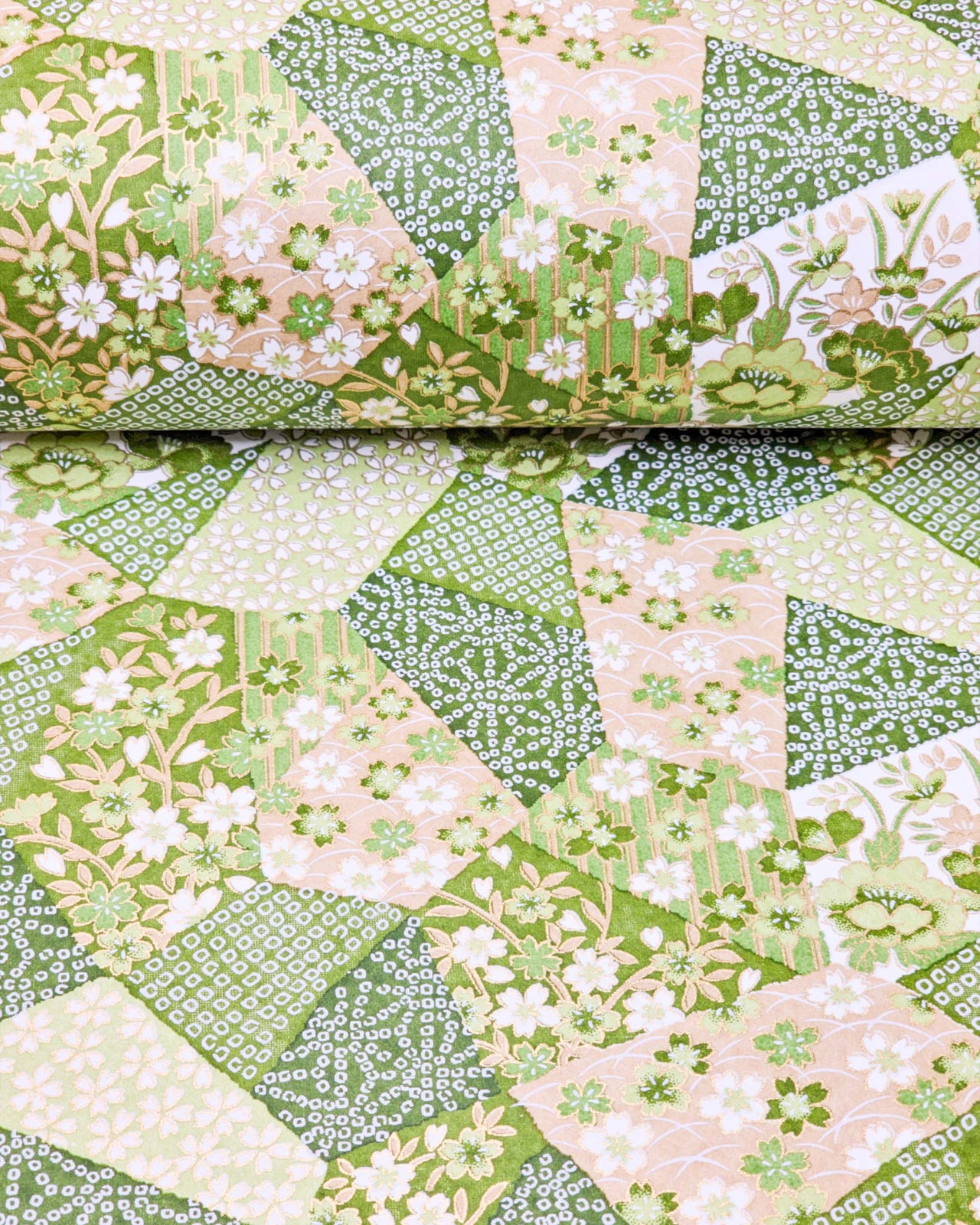 Japanese chiyogami paper featuring green, beige, and white floral patches embedded with assorted geometric and floral designs with metallic gold details, shown rolled to highlight the design.