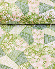 Japanese chiyogami paper featuring green, beige, and white floral patches embedded with assorted geometric and floral designs with metallic gold details, shown rolled to highlight the design.