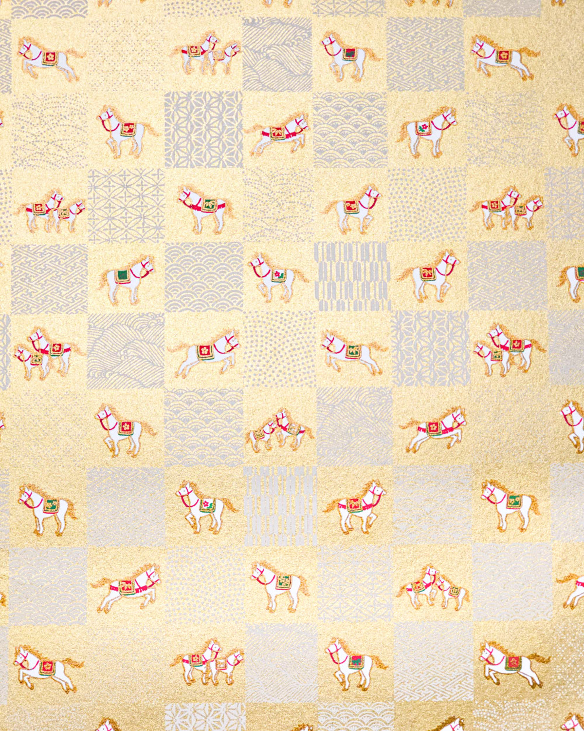 Japanese chiyogami paper featuring white horses with gold manes wearing red and green saddles and bridles, alternating with assorted white traditional Japanese patterns in an ichimatsu (checker) design on a metallic gold background.