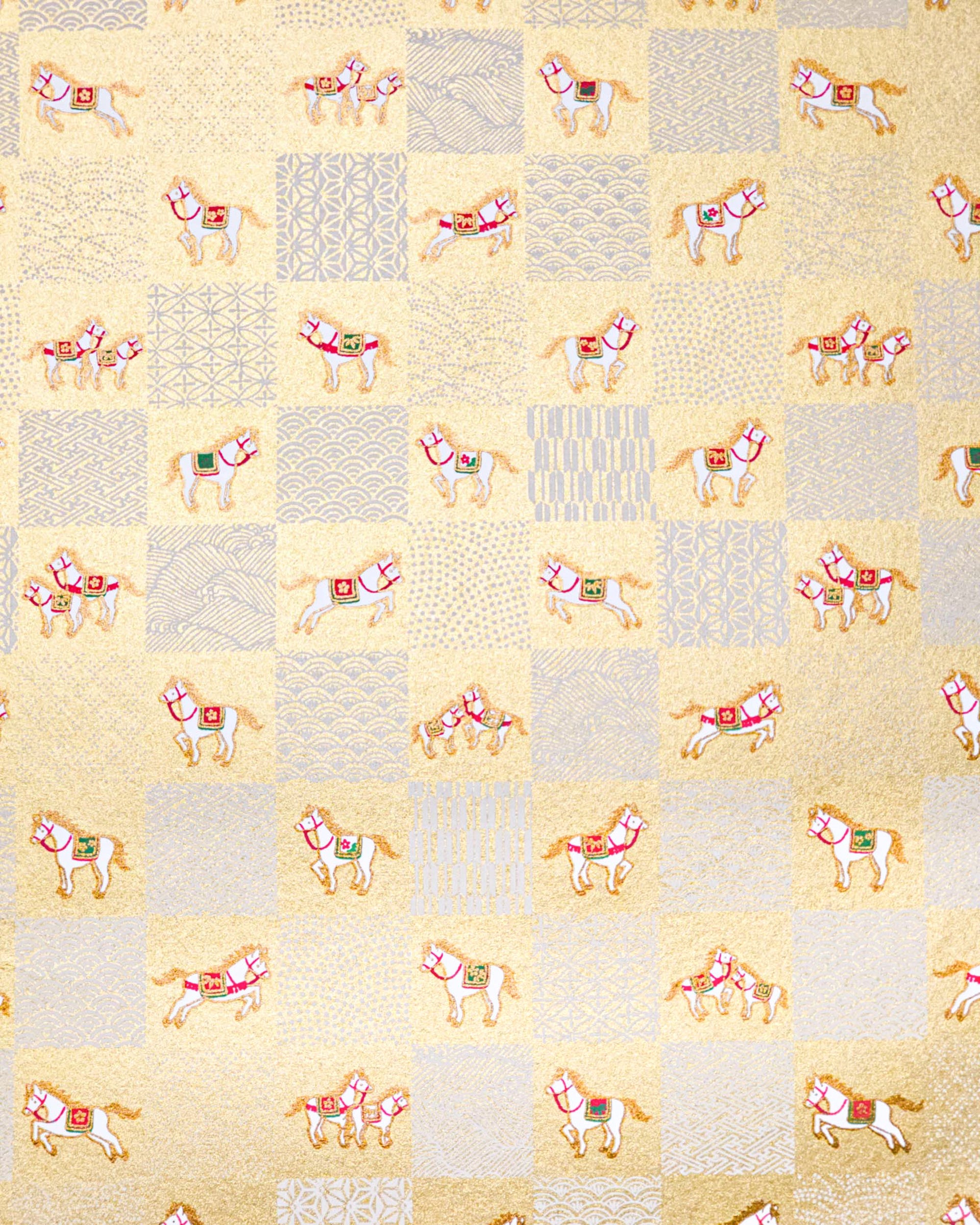 Japanese chiyogami paper featuring white horses with gold manes wearing red and green saddles and bridles, alternating with assorted white traditional Japanese patterns in an ichimatsu (checker) design on a metallic gold background.