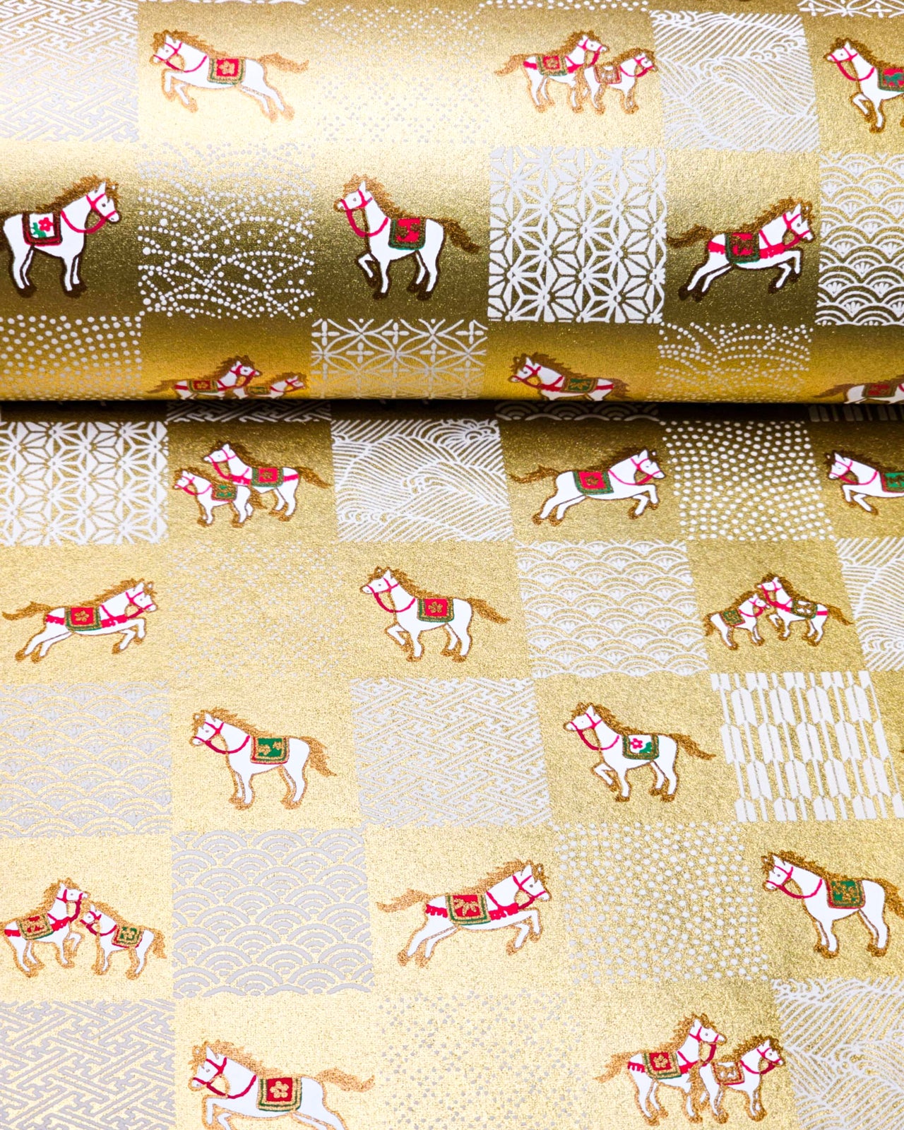 Japanese chiyogami paper featuring white horses with red and green accents and white assorted traditional Japanese designs in an ichimatsu (checker) design on a metallic gold background.