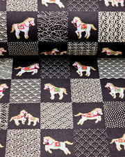 Japanese chiyogami paper featuring white horses with red and green accents and beige assorted traditional Japanese designs in an ichimatsu (checker) design on a black background with metallic gold accents.