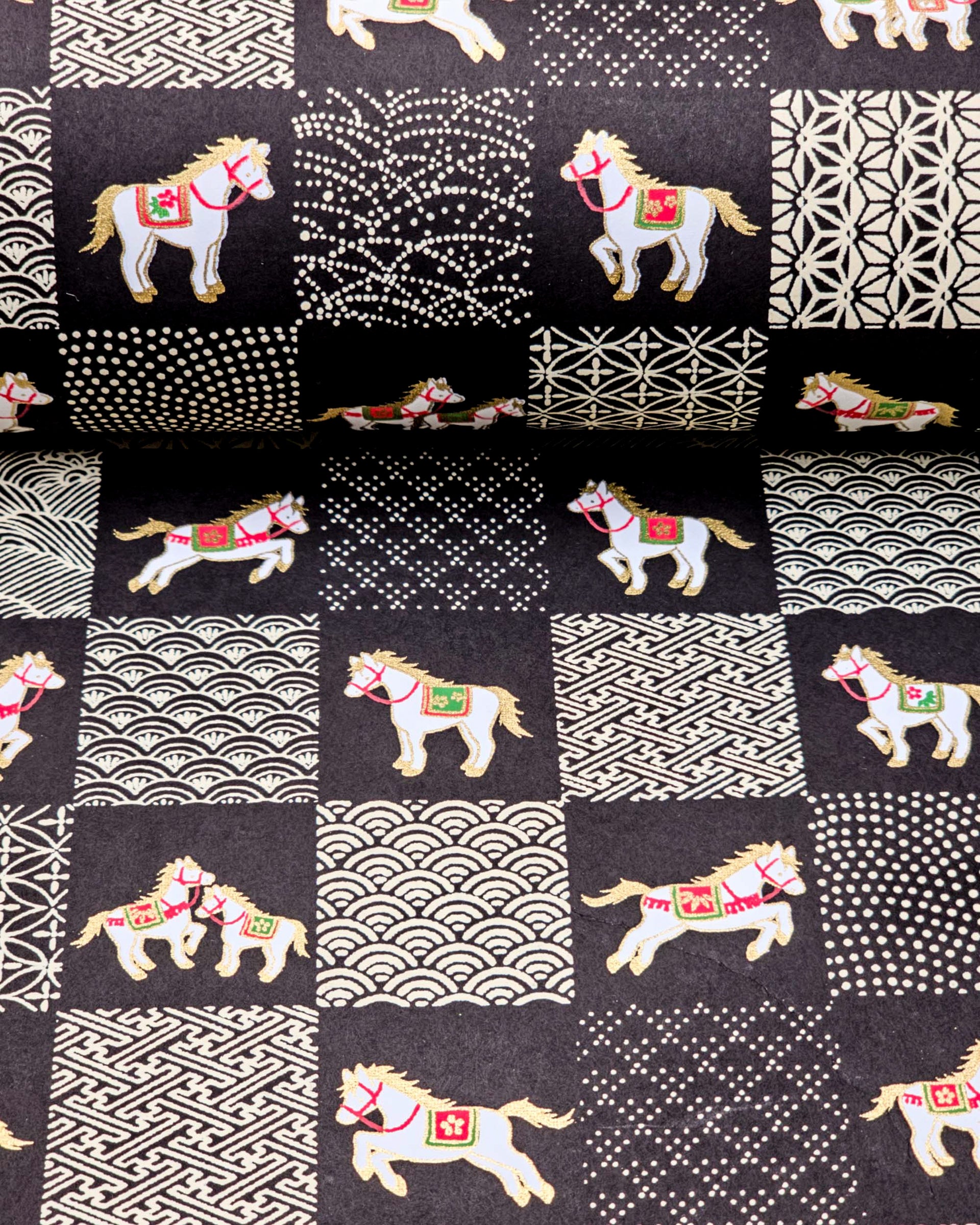 Japanese chiyogami paper featuring white horses with red and green accents and beige assorted traditional Japanese designs in an ichimatsu (checker) design on a black background with metallic gold accents.