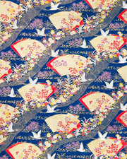 Japanese chiyogami paper featuring white flying cranes, gold and red folding fans, and assorted red, purple, white, and yellow flowers on a dark blue background with metallic gold wave and geometric details.