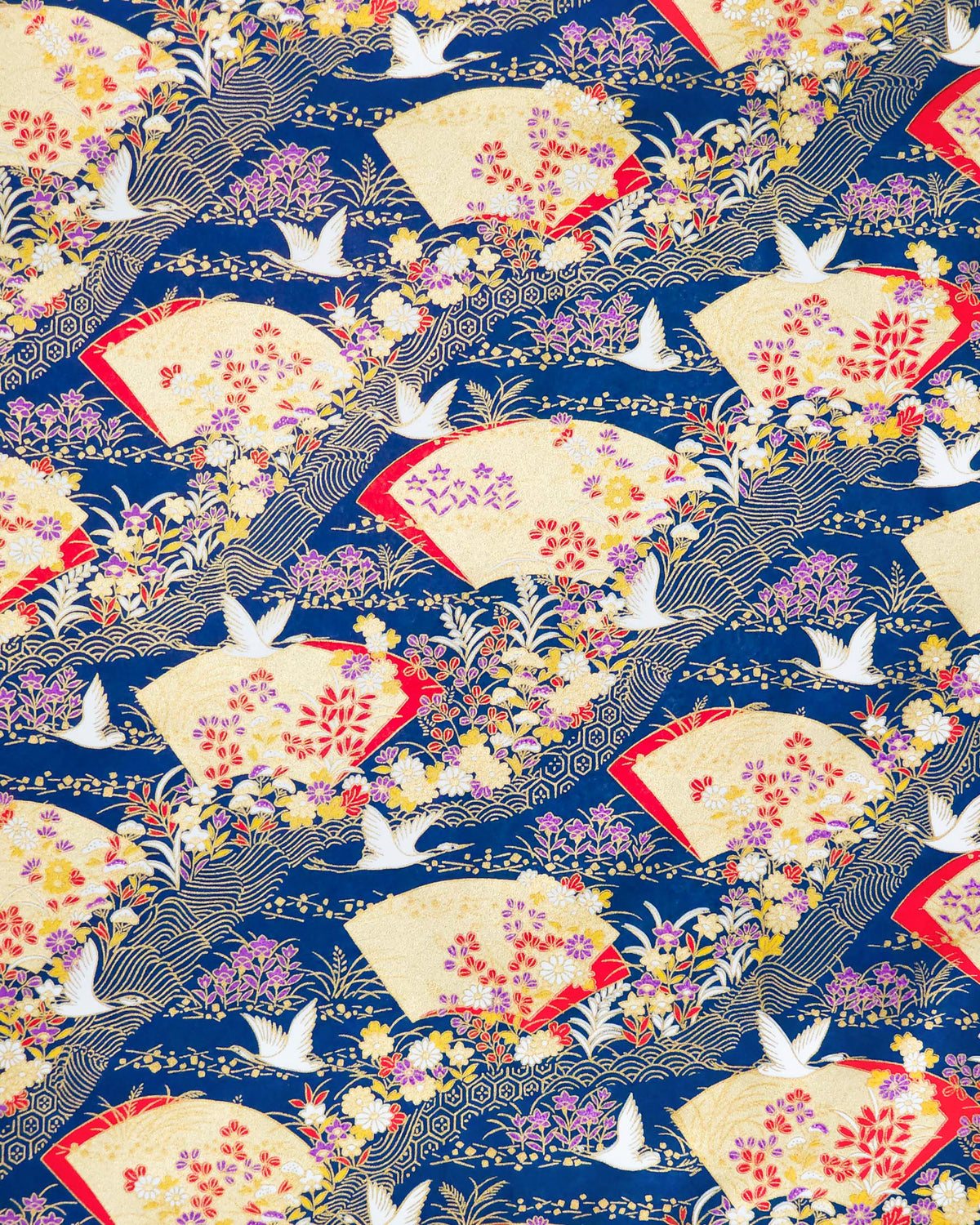 Japanese chiyogami paper featuring white flying cranes, gold and red folding fans, and assorted red, purple, white, and yellow flowers on a dark blue background with metallic gold wave and geometric details.
