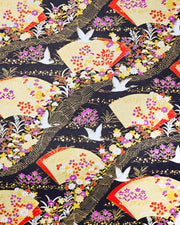 Japanese chiyogami paper featuring white flying cranes, gold and red folding fans, and assorted red, purple, white, and yellow flowers on a black background with metallic gold wave and geometric details.