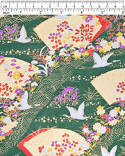 Japanese chiyogami paper featuring white flying cranes, gold and red folding fans, and assorted red, purple, white, and yellow flowers on a green background with metallic gold wave and geometric details, shown next to a ruler for size reference.
