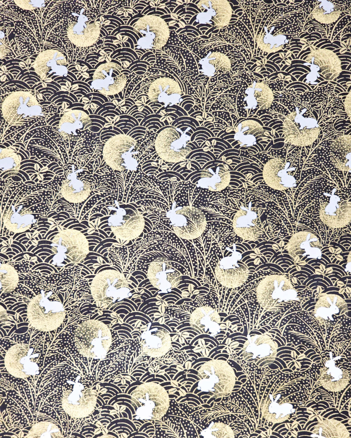 Japanese chiyogami paper featuring white rabbits with metallic gold moons, waves, and hagi bush clover on a black background.