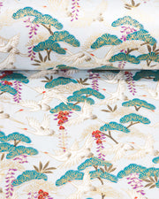 Japanese chiyogami paper featuring white flying cranes, purple and red wisteria, and green pine on a pearlescent light blue background with metallic gold details, shown rolled to highlight the design.