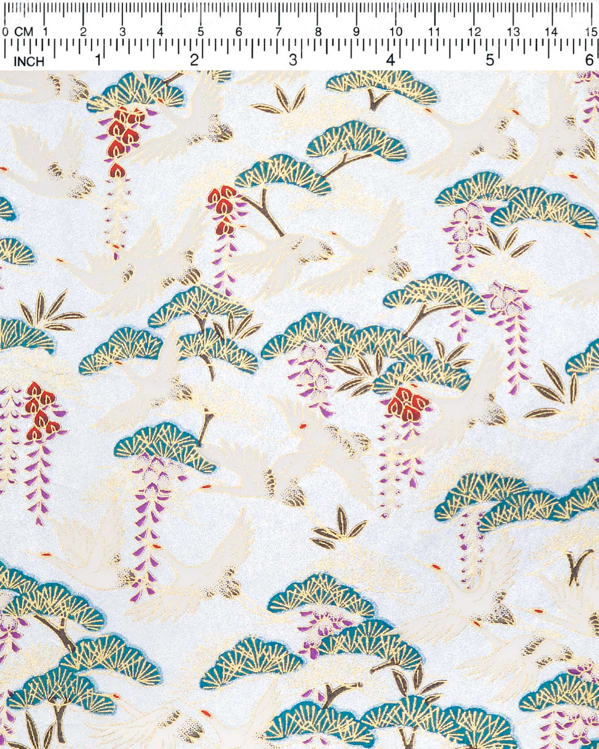 Japanese chiyogami paper featuring white flying cranes, purple and red wisteria, and green pine on a pearlescent light blue background with metallic gold details, shown next to a ruler for size reference.