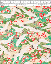 Japanese chiyogami paper featuring white flying cranes and red and white cherry blossoms among beige and green clouds and green waves with metallic gold details, shown next to a ruler for size reference.