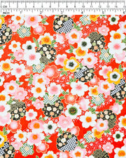Japanese chiyogami paper featuring pink, white, and orange cherry blossoms with green leaves and black yukiwa (snowflake) on a red background with metallic gold details, shown next to a ruler for size reference.