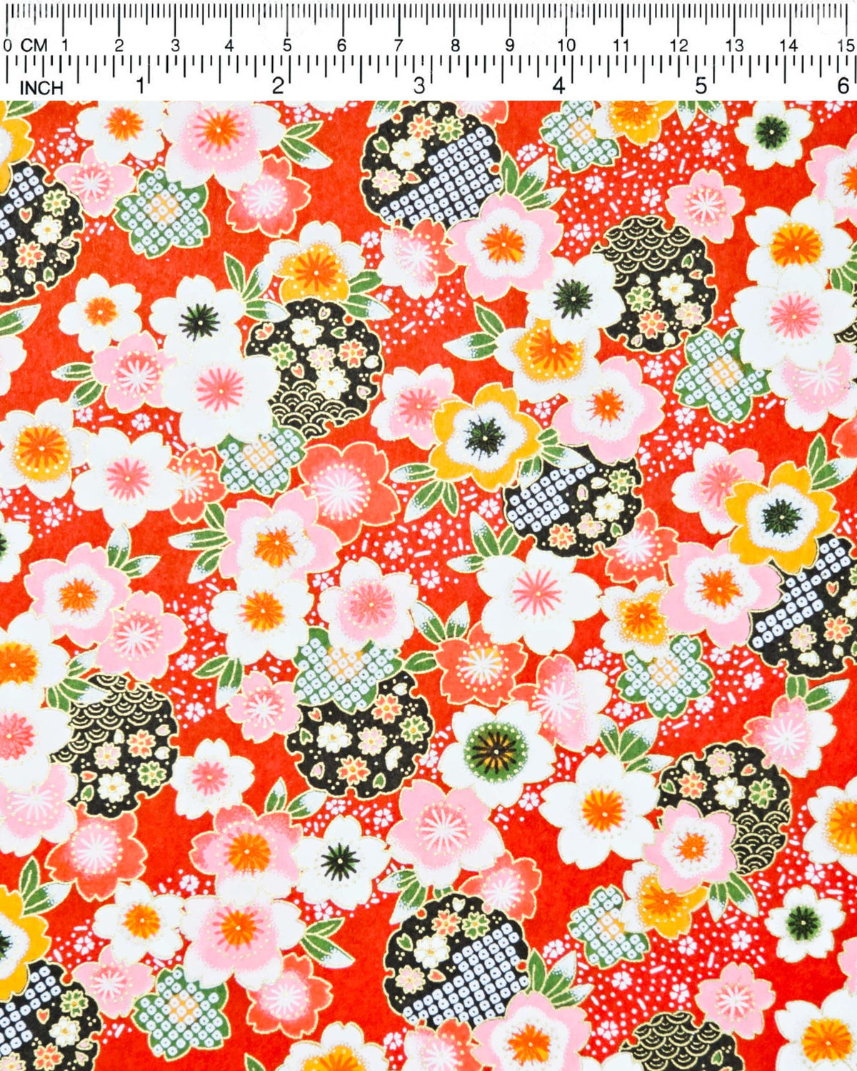 Japanese chiyogami paper featuring pink, white, and orange cherry blossoms with green leaves and black yukiwa (snowflake) on a red background with metallic gold details, shown next to a ruler for size reference.