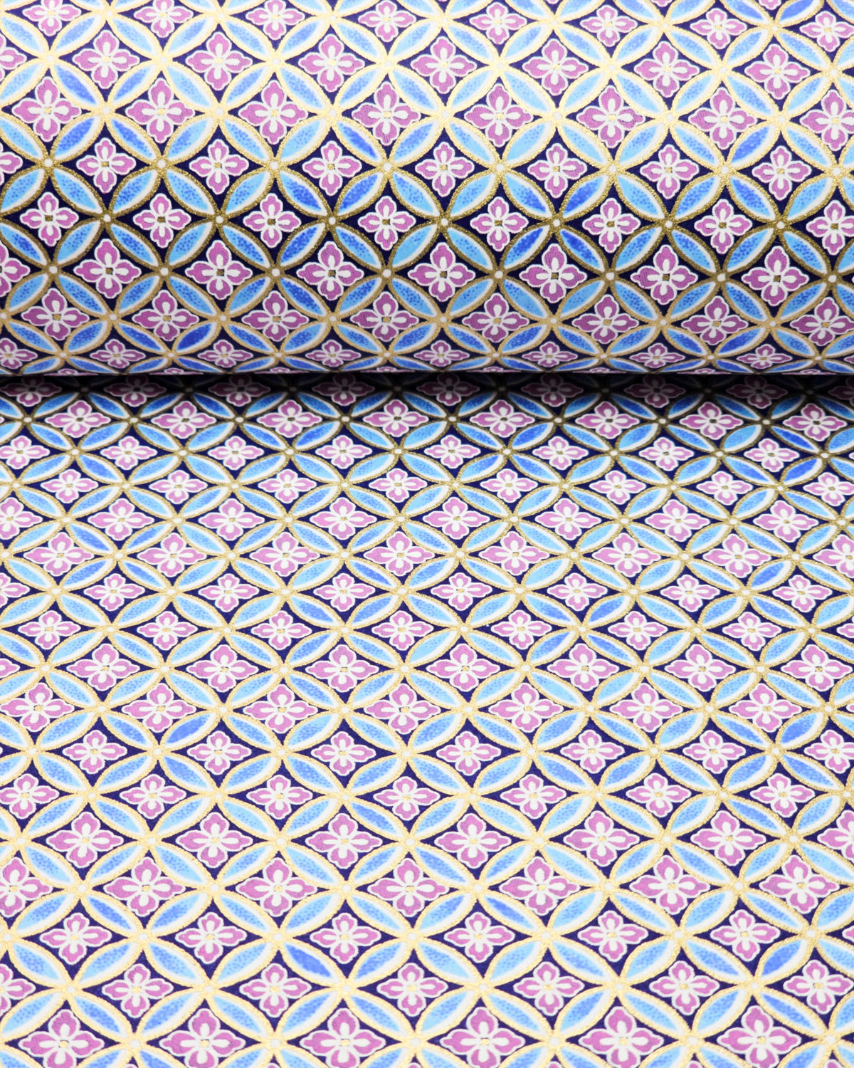 Japanese chiyogami paper featuring a blue and metallic gold shippo pattern with purple and white hanabishi (flower diamond) pattern in the center on a black background, shown rolled to highlight the design.