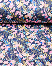 Japanese chiyogami paper featuring ypink and yellow plum blossoms and blue, pink, and yellow wisteria on a dark blue background with metallic gold details, shown rolled to highlight the design.