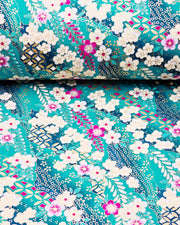 Japanese chiyogami paper featuring cream and magenta pink plum blossoms and cream, magenta pink, and teal wisteria on a teal blue background with metallic gold details, shown rolled to highlight the design.