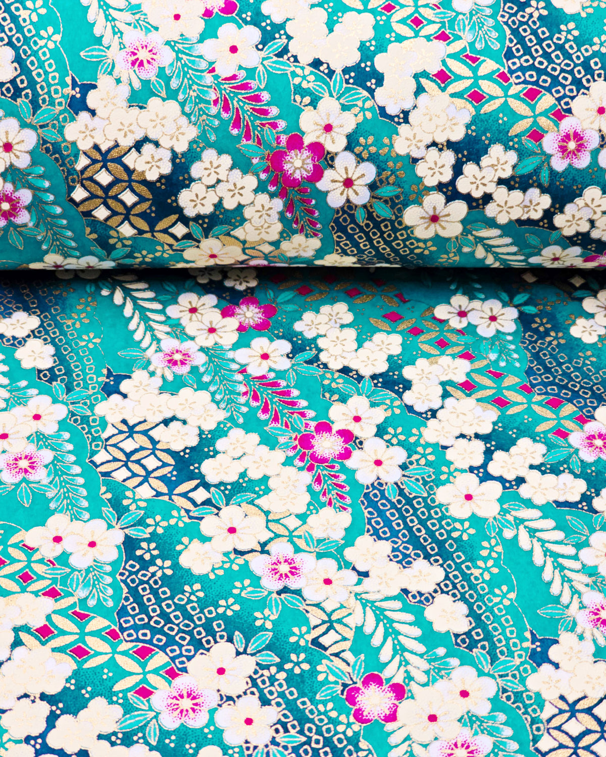 Japanese chiyogami paper featuring cream and magenta pink plum blossoms and cream, magenta pink, and teal wisteria on a teal blue background with metallic gold details, shown rolled to highlight the design.