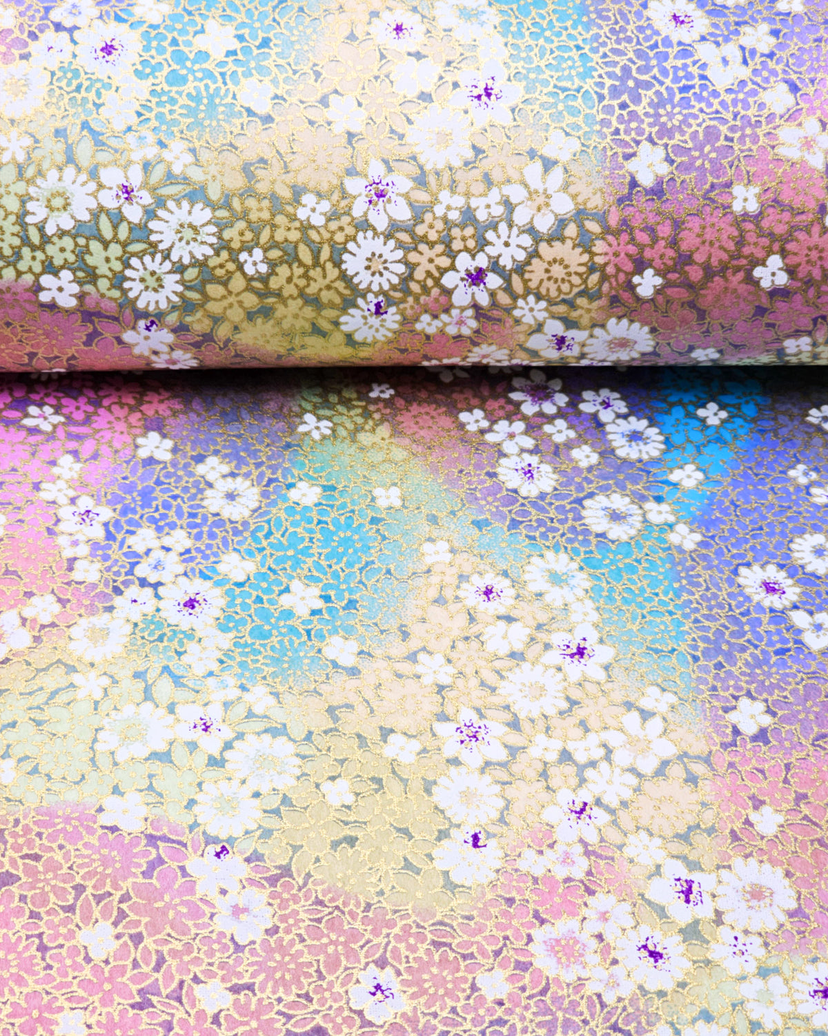 Japanese chiyogami paper featuring small white and pastel rainbow-colored flowers with metallic gold details, shown rolled to highlight the design.