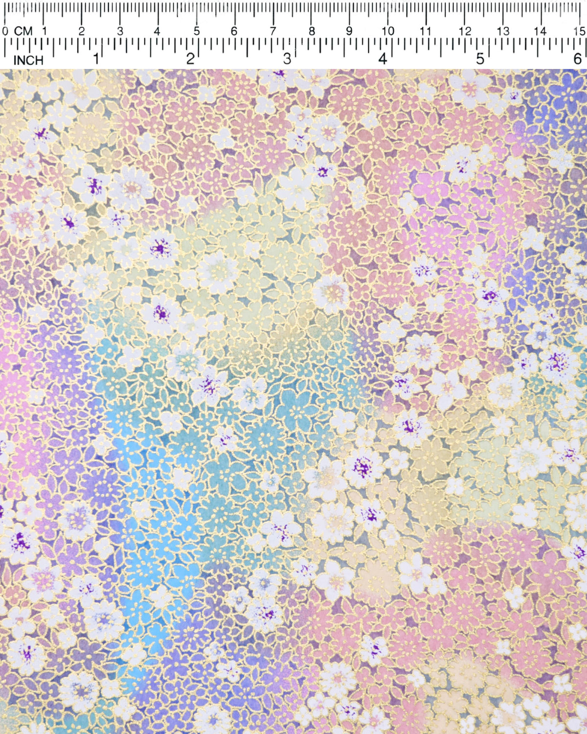 Japanese chiyogami paper featuring small white and pastel rainbow-colored flowers with metallic gold details, shown next to a ruler for size reference.