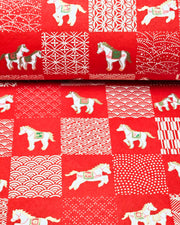 Japanese chiyogami paper featuring white horses with red and green accents and white assorted traditional Japanese designs in an ichimatsu (checker) design on a red background with metallic gold accents.