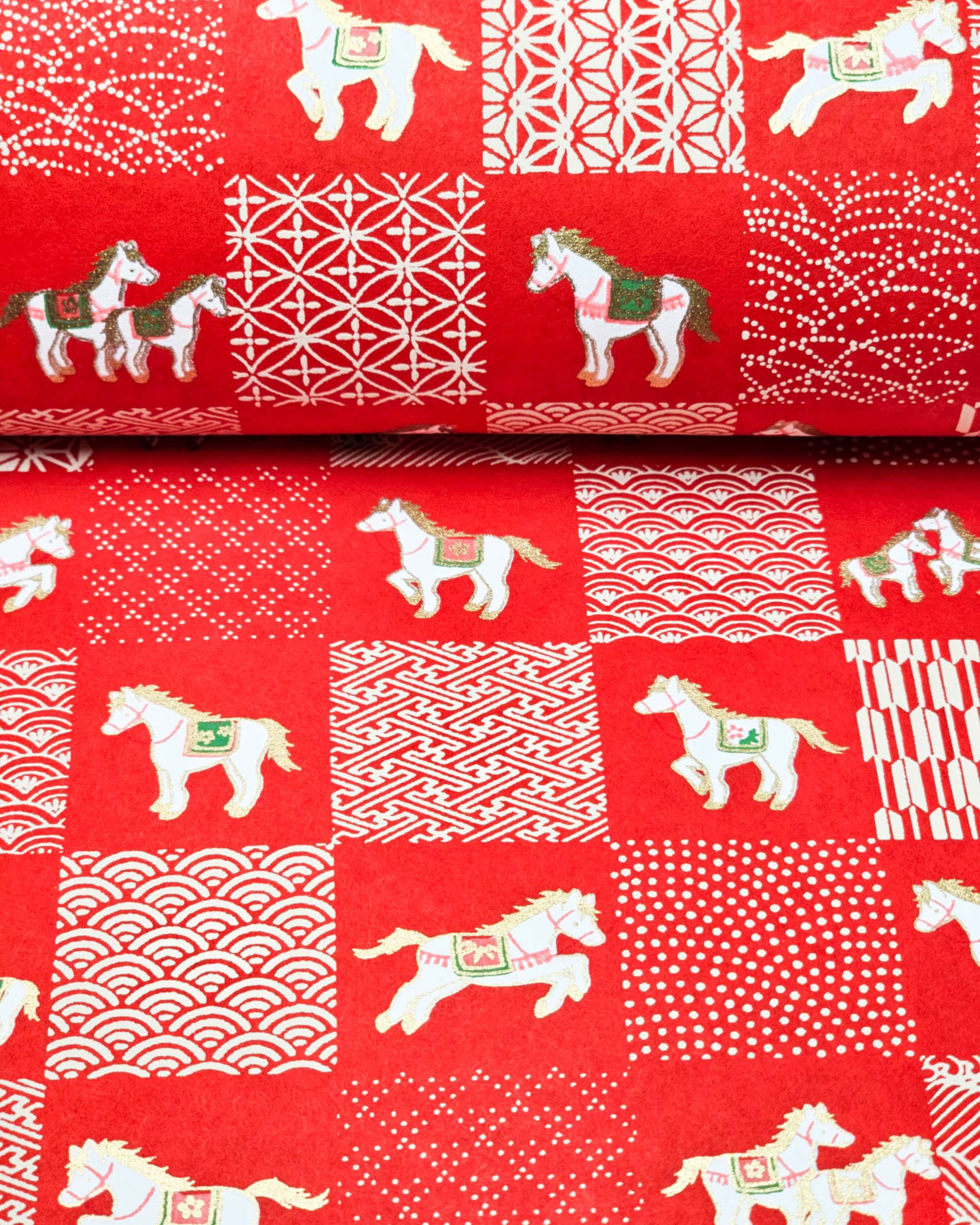 Japanese chiyogami paper featuring white horses with red and green accents and white assorted traditional Japanese designs in an ichimatsu (checker) design on a red background with metallic gold accents.