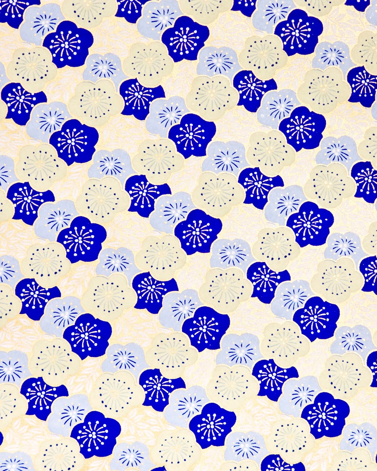 Japanese chiyogami paper featuring large dark blue, light blue, and off-white plum blossoms on a metallic gold background.