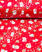 Japanese chiyogami paper featuring assorted white and red Maneki Neko (lucky cats) with small white and gold cherry blossoms and temari balls on a bright red background with metallic gold details.