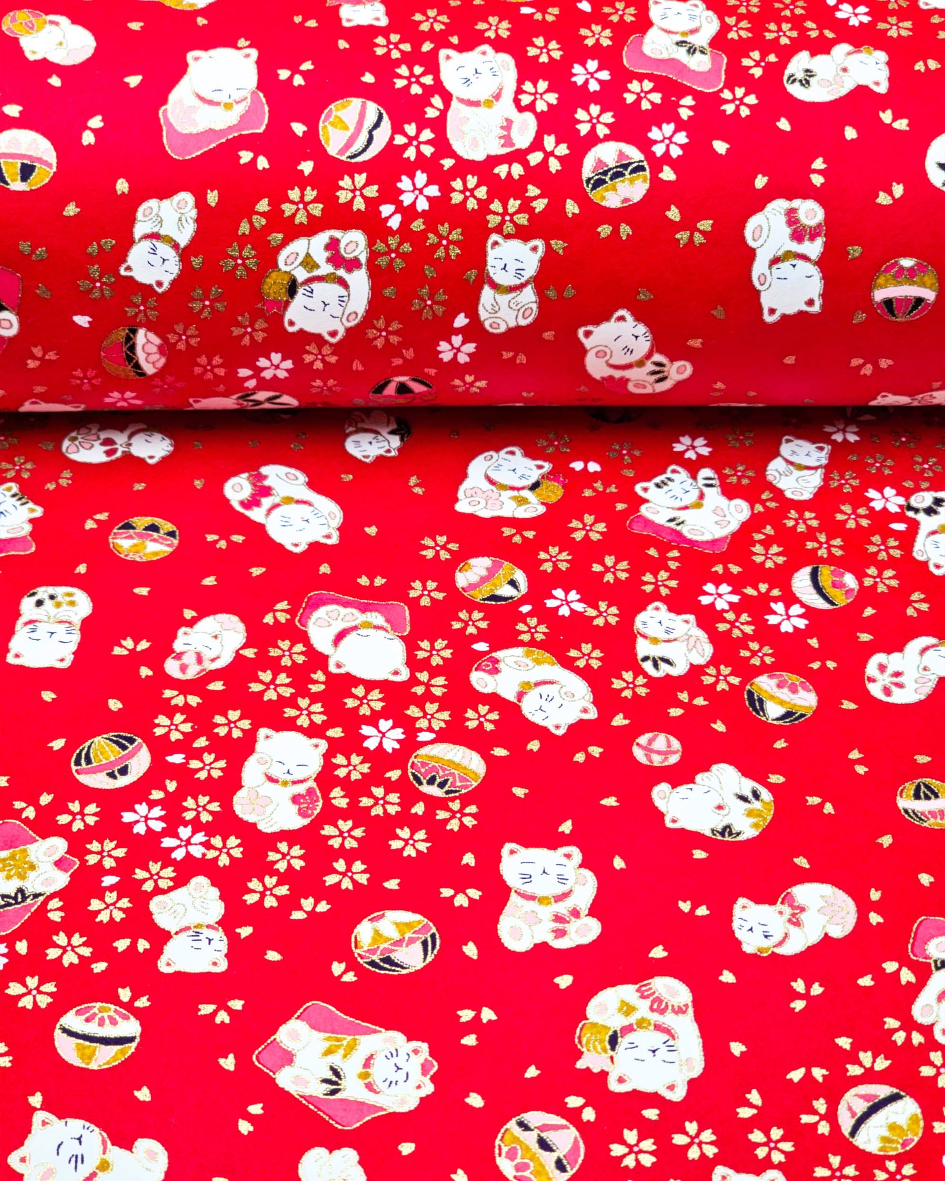 Japanese chiyogami paper featuring assorted white and red Maneki Neko (lucky cats) with small white and gold cherry blossoms and temari balls on a bright red background with metallic gold details.