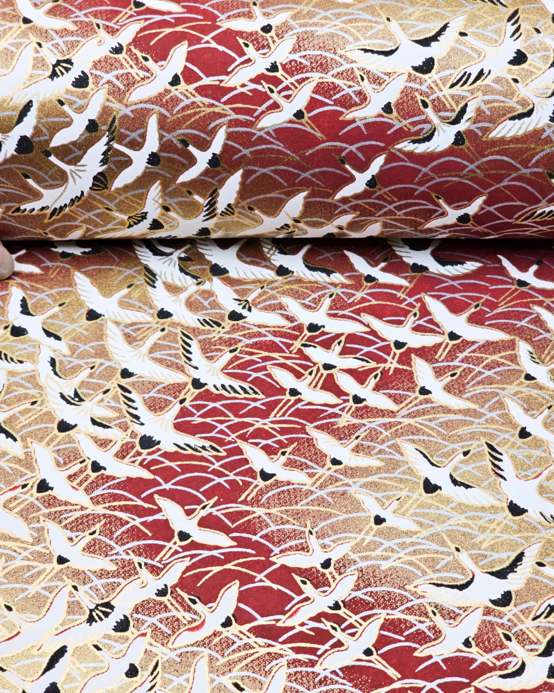 Japanese chiyogami paper featuring white flying cranes in a zigzag formation on a brown background with metallic gold and silver details.