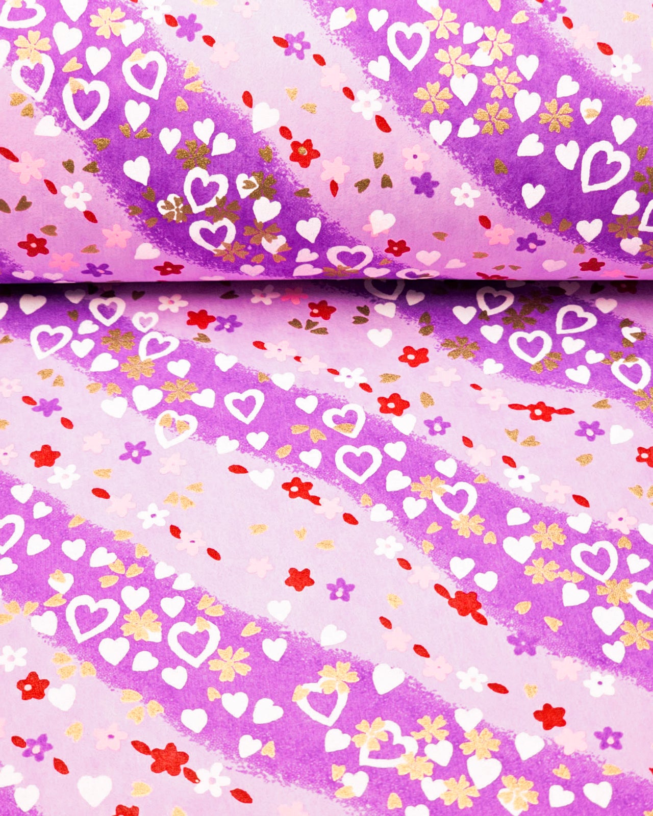 Japanese chiyogami paper featuring white hearts, small pink, red, and purple flowers, and metallic gold blossoms on a purple gradient background.