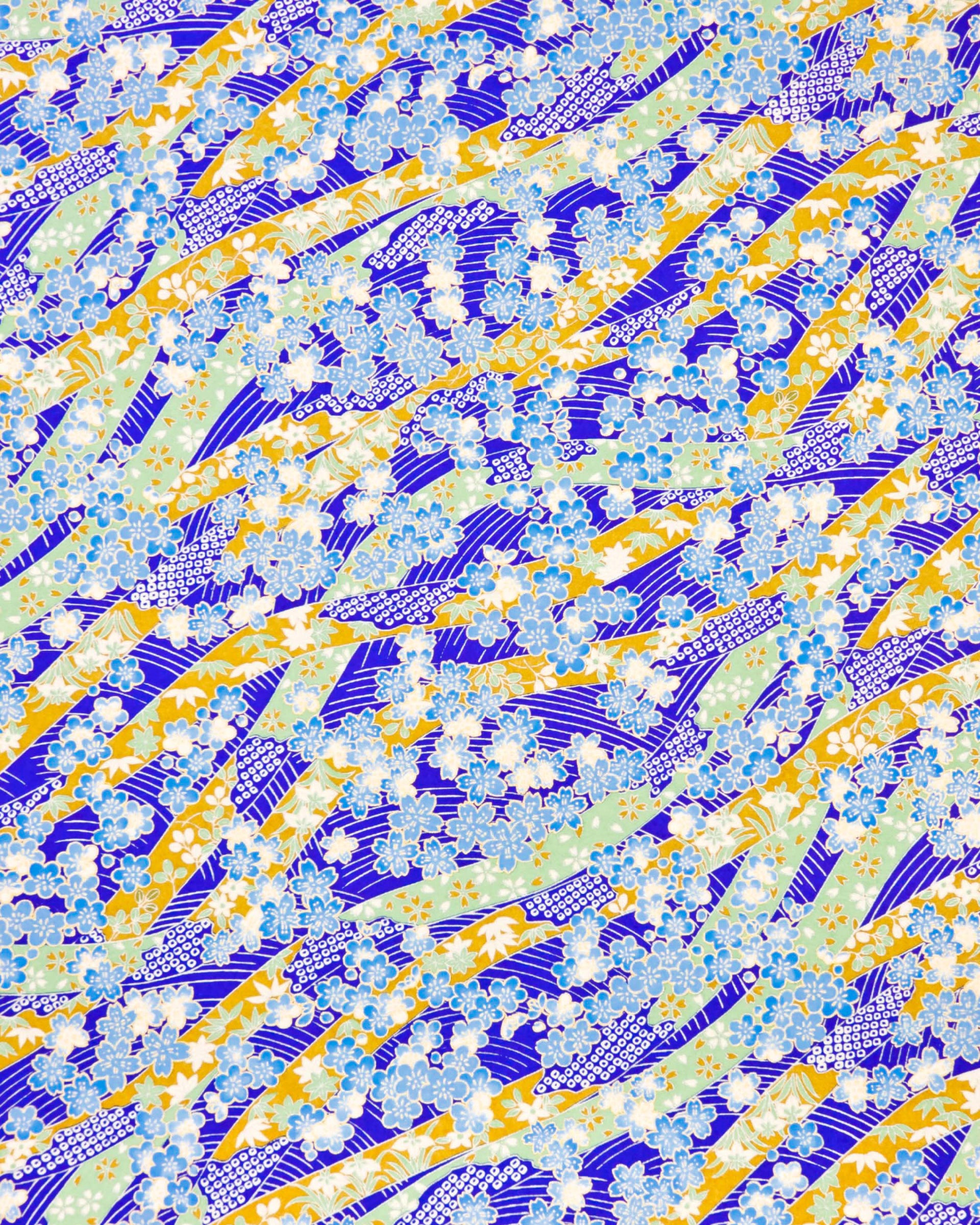 Japanese chiyogami paper featuring blue plum and cherry blossoms with flowing green and brown ribbons on a dark vibrant blue and silver  seigaihai background with metallic gold details.