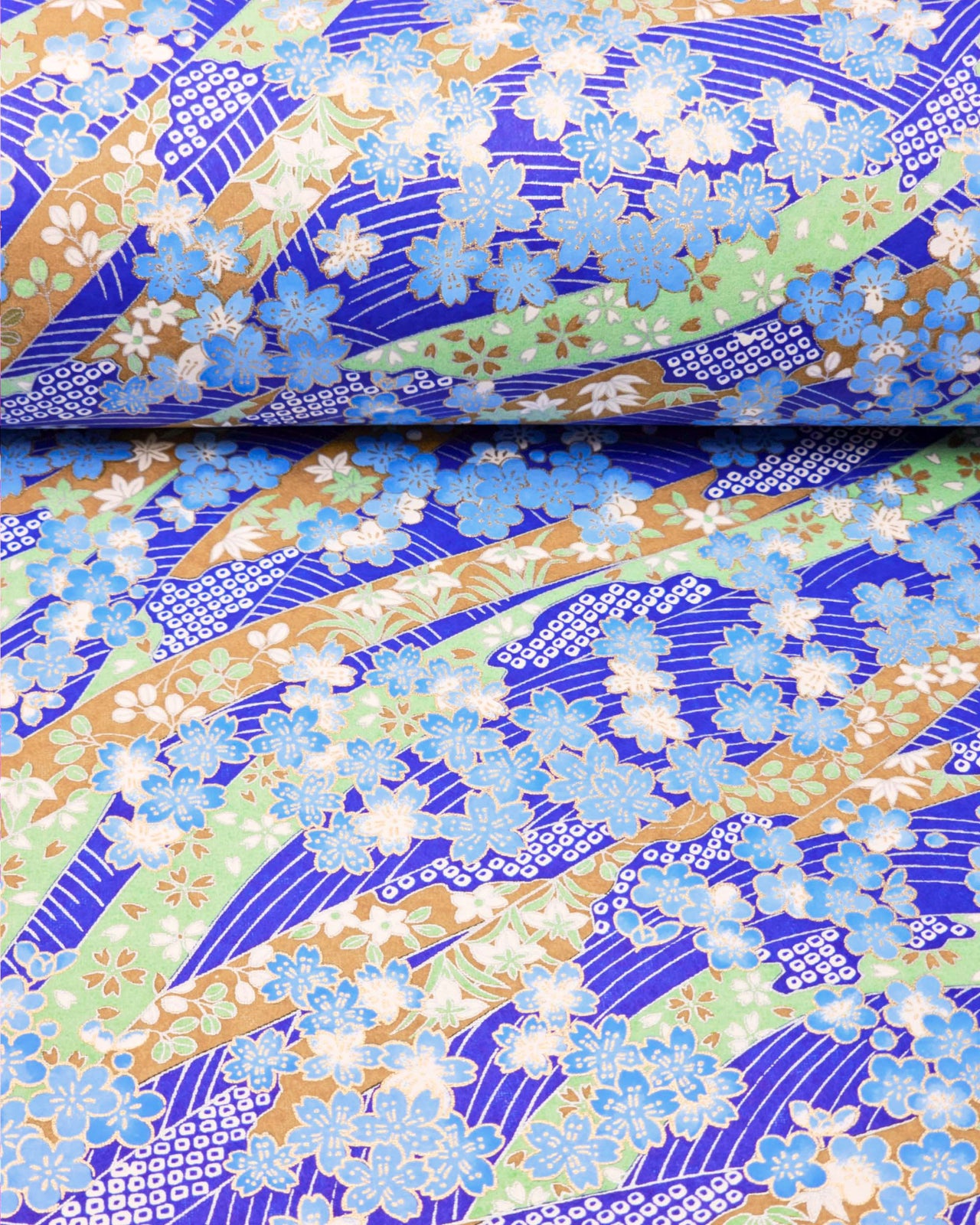 Japanese chiyogami paper featuring blue plum and cherry blossoms with flowing green and brown ribbons on a dark vibrant blue and silver seigaihai background with metallic gold details.